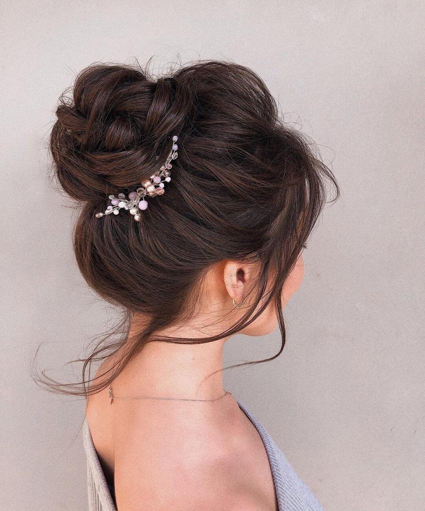 Chignon alto e morbido con delicati intrecci e gioiello prezioso