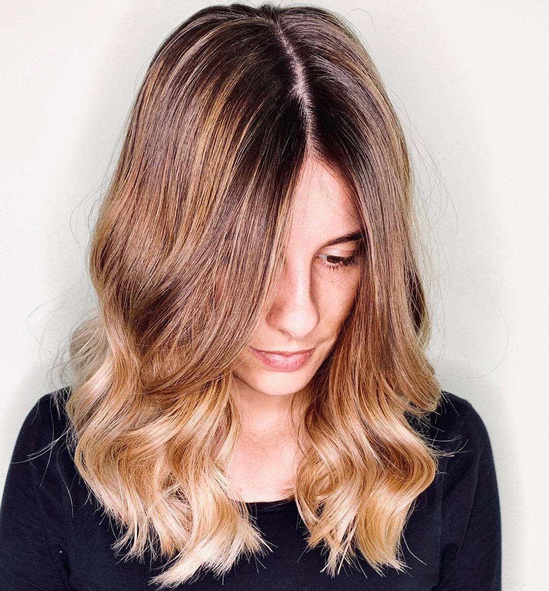 Capelli di media lunghezza, mossi e con riga nel mezzo arricchiti da shatush biondo